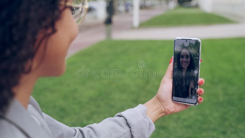 Achteraanzicht van een vrouw die videogesprekken voert met een mooie jonge zakenvrouw terwijl ze koffie op straat houdt.