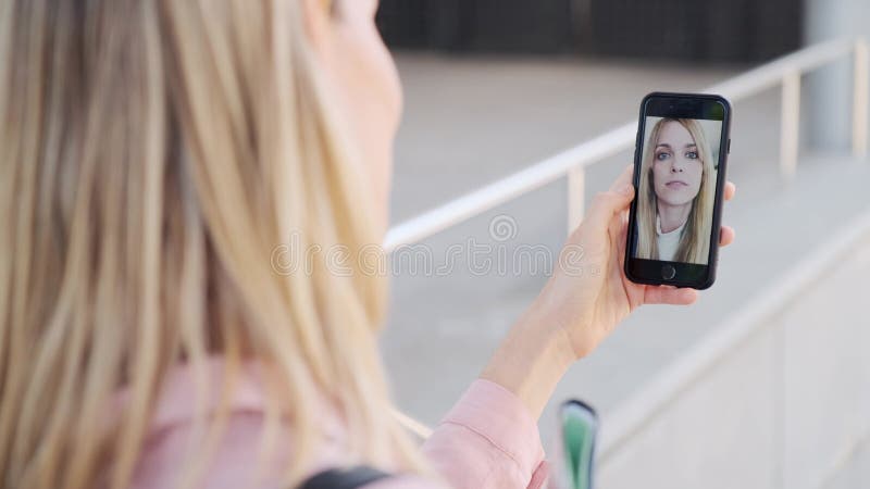 Achteraanzicht van vrouw die videogesprekken voert met een mooie jonge zakenvrouw terwijl ze op straat blijft.