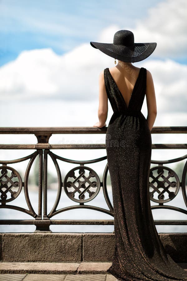 Woman Back Side View in Hat and Evening Dress Outdoor. Fashion Model Rear View looking away. Luxury Lady in long Gown at Promenade looking at Sky. Woman Back Side View in Hat and Evening Dress Outdoor. Fashion Model Rear View looking away. Luxury Lady in long Gown at Promenade looking at Sky