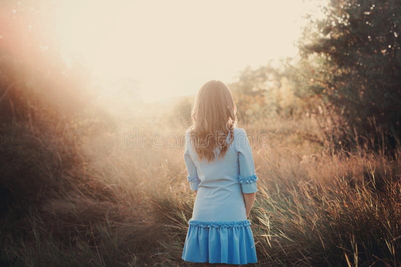 Achtermening van een mooi jong vrouw of meisje die op zeer groene weide op de zonsondergang een letten stock afbeeldingen Achtermening van een mooi jong vrouw of meisje die op zeer groene weide op de zonsondergang een letten stock afbeeldingen