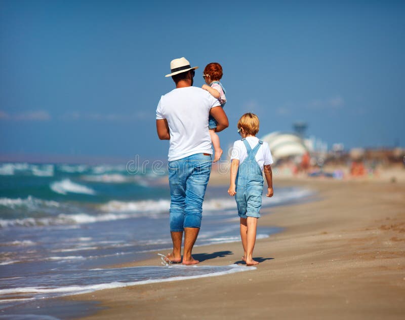 Achtermening van familie, vader met jonge geitjes die op zandig strand dichtbij het overzees lopen, de zomervakantie stock afbeelding Achtermening van familie, vader met jonge geitjes die op zandig strand dichtbij het overzees lopen, de zomervakantie stock afbeelding