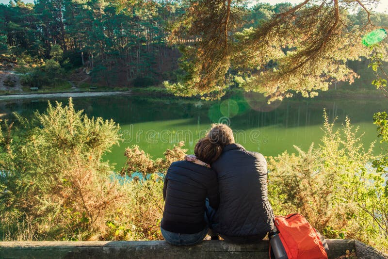 Achtermening van mooie van de paarman en vrouw zitting dichtbij bos en meer die koesteren ontspannen De Openluchtconcepten van li stock foto Achtermening van mooie van de paarman en vrouw zitting dichtbij bos en meer die koesteren ontspannen De Openluchtconcepten van li stock foto