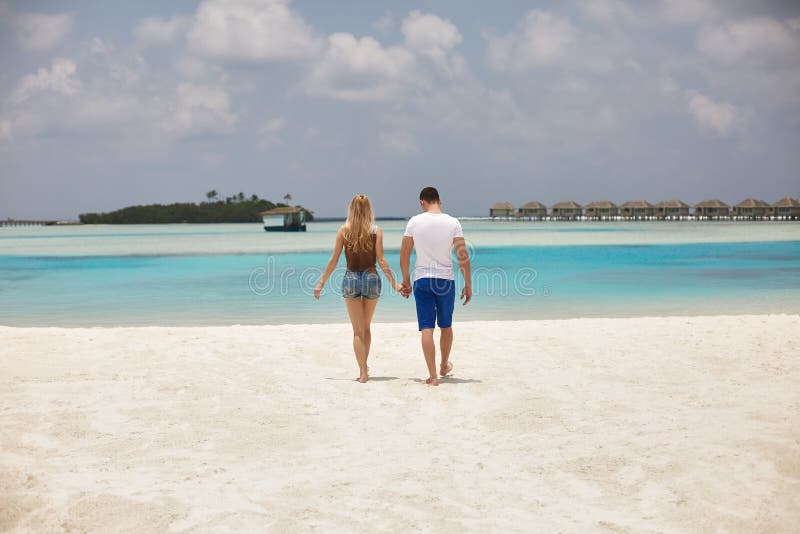 Achtermening van paarholding handen en het lopen aan de blauwe oceaanlagune op de Maldiven bij luxury spa toevlucht Reis en royalty-vrije stock foto's Achtermening van paarholding handen en het lopen aan de blauwe oceaanlagune op de Maldiven bij luxury spa toevlucht Reis en royalty-vrije stock foto's