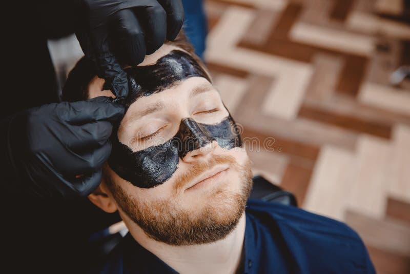 Acne removal with cosmetic product, cleaning pores of man skin, barber applying black charcoal mask to client man in spa salon. Acne removal with cosmetic product, cleaning pores of man skin, barber applying black charcoal mask to client man in spa salon.