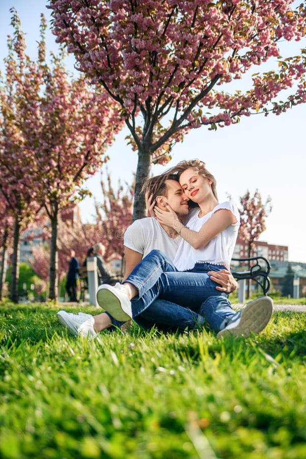 Acople abraços perto das árvores de sakura no jardim de florescência Os pares no amor passam o tempo no jardim da mola, flores no foto de stock Acople abraços perto das árvores de sakura no jardim de florescência Os pares no amor passam o tempo no jardim da mola, flores no foto de stock