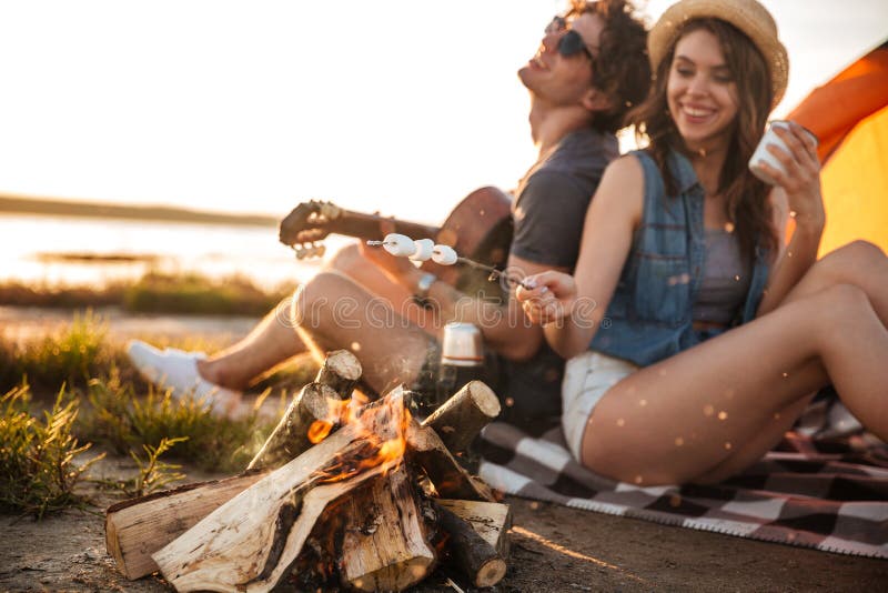 Acople o jogo da guitarra e a fritura de marshmallows na fogueira imagens de stock royalty free Acople o jogo da guitarra e a fritura de marshmallows na fogueira imagens de stock royalty free