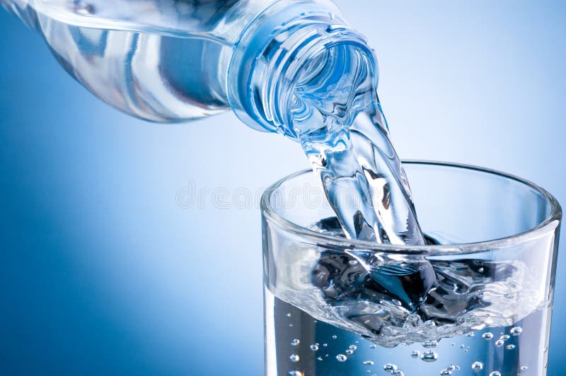 Acqua di versamento dalla bottiglia in vetro su fondo blu