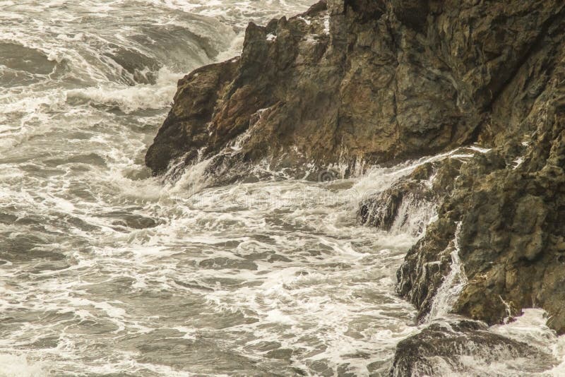 Acqua spumosa turbolenta che turbina intorno e che spruzza su sulle rupe rocciose nell'oceano - naturalmente monocromatico fotografie stock Acqua spumosa turbolenta che turbina intorno e che spruzza su sulle rupe rocciose nell'oceano - naturalmente monocromatico fotografie stock