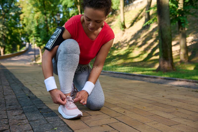 Activa atleta afroamericana de mediana edad atando cordones de zapatos preparándose para correr por el parque forestal en un cálid. Una mujer activa de mediana edad corredora atleta afroamericana atando cordones de zapatos preparándose para correr por el parque forestal en un cálido día soleado de verano. deporte activo estilo de vida saludable jogging