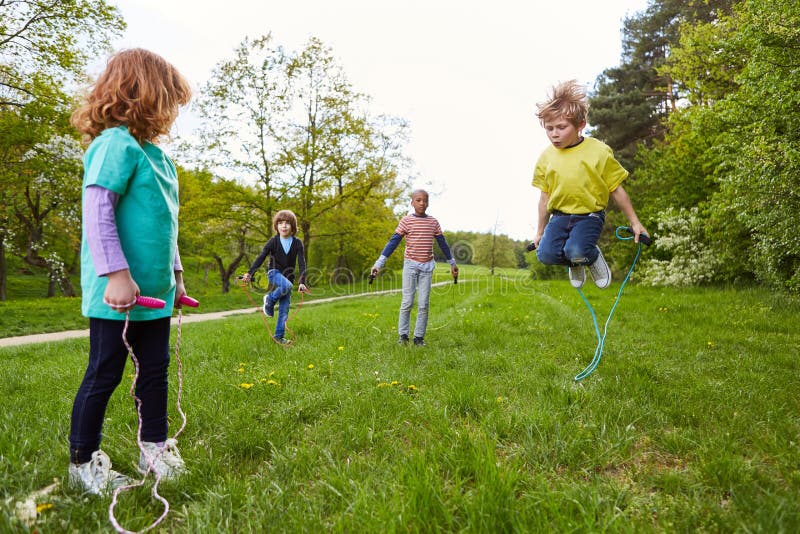 Active children play jump rope in the park together in the summer in a meadow