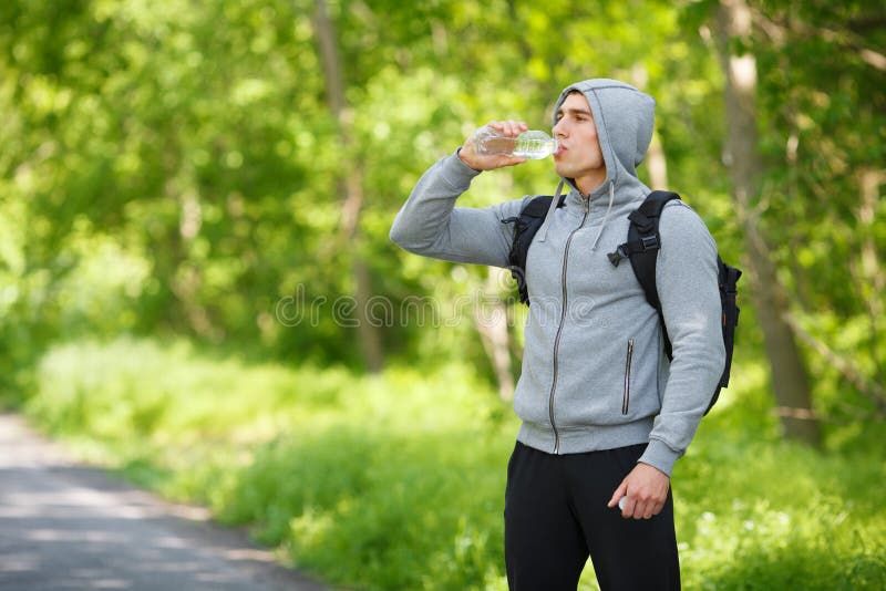 Active man drinking water from a bottle, outdoor. Young muscular male quenches thirst