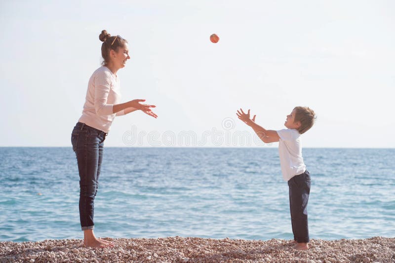 Active mother female and happy small kid playing leisure games on sea beach throwing apple in air in spring