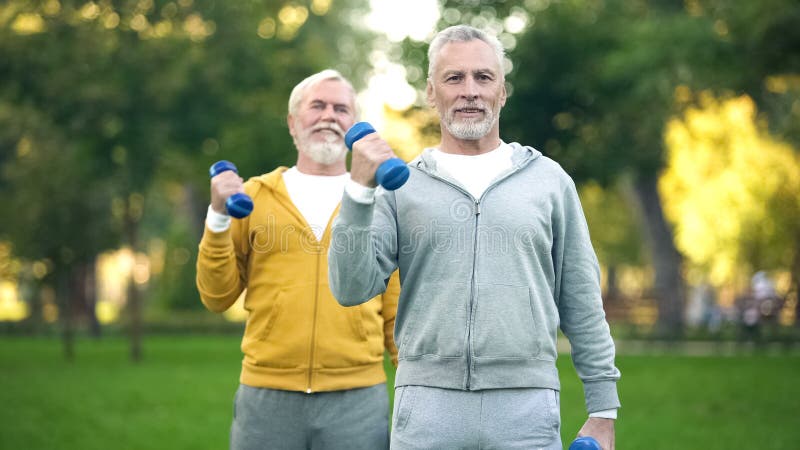 Active retired friends lifting dumbbells, fitness training park, healthy aging royalty free stock image Active retired friends lifting dumbbells, fitness training park, healthy aging royalty free stock image