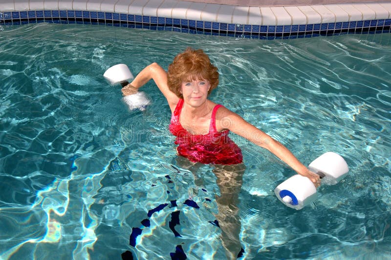 Atraktivní usmívající se senior žena dělá cvičení v bazénu.