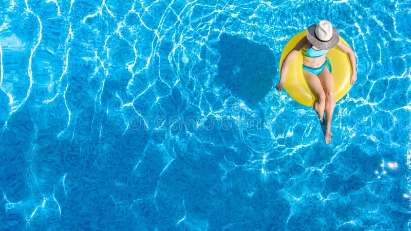 Active young girl in swimming pool aerial top view from above, child relaxes and swims on inflatable ring donut and has fun in water on family vacation, tropical holiday resort