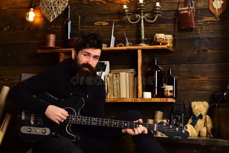 Actividad preferida El músico barbudo del hombre goza el igualar con la guitarra baja, fondo de madera Individuo en atmósfera cal foto de archivo libre de regalías Actividad preferida El músico barbudo del hombre goza el igualar con la guitarra baja, fondo de madera Individuo en atmósfera cal foto de archivo libre de regalías