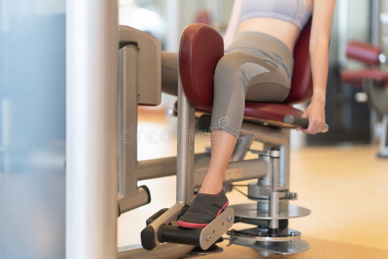 Adatta una donna che usa la macchina del peso per le sue gambe in palestra fotografia stock Adatta una donna che usa la macchina del peso per le sue gambe in palestra fotografia stock