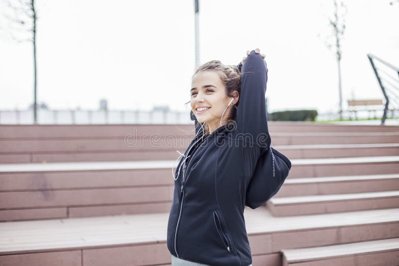 Adatta una giovane donna con le cuffie che fa esercizi di allungamento sulle scale all'aperto fotografia stock