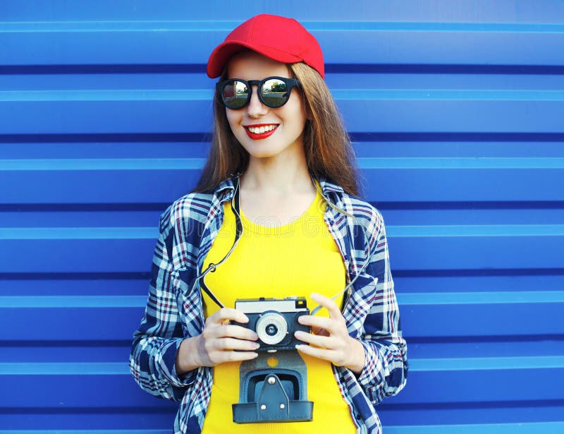 Adatti ad uso abbastanza sorridente della ragazza i vestiti variopinti con la retro macchina fotografica sopra il blu immagine stock libera da diritti Adatti ad uso abbastanza sorridente della ragazza i vestiti variopinti con la retro macchina fotografica sopra il blu immagine stock libera da diritti