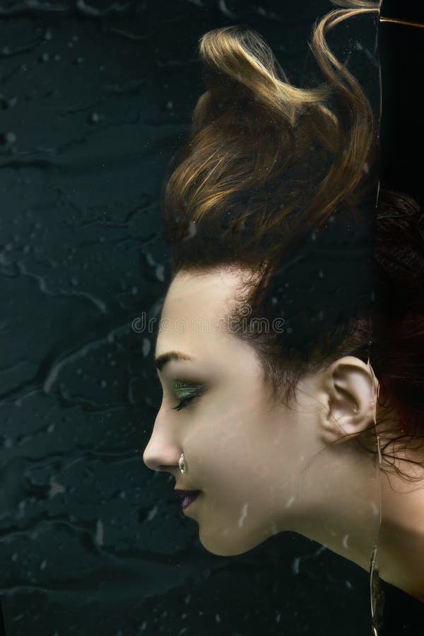 Fashion portrait of beautiful girl peering behind the glass,young woman face profile under the water,creative idea, the concept of uniqueness, beauty and style. Fashion portrait of beautiful girl peering behind the glass,young woman face profile under the water,creative idea, the concept of uniqueness, beauty and style