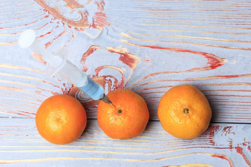 Added mandarin with a syringe. Background wooden in the old stele. in a syringe blue liquid. Chemical experiments in the food stock photo Added mandarin with a syringe. Background wooden in the old stele. in a syringe blue liquid. Chemical experiments in the food stock photo