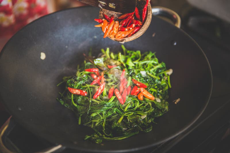 Adding sliced red pepper into water spinach stir-fry, close up
