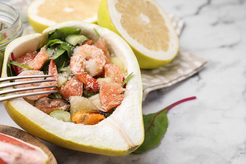 Adekvat pomelosallad med räkor i hälften av frukt på vit marmor i bordsduk. utrymme för text arkivbild