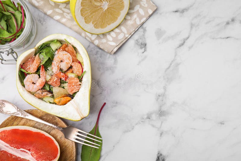 Adekvat pomelosallad med räkor i hälften av frukten på det vita marmorbordet med plant lägg. utrymme för text arkivfoto