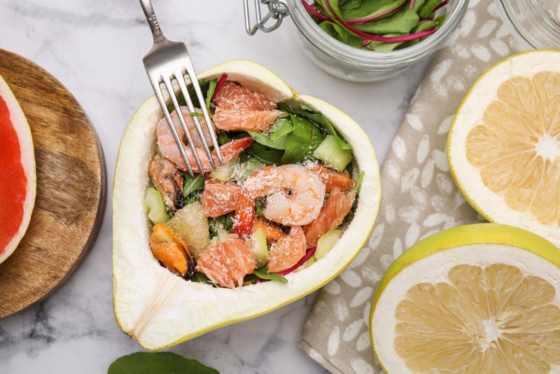Adekvat pomelosallad med räkor i hälften av frukten på det vita marmorbordet med plant lägg royaltyfria foton