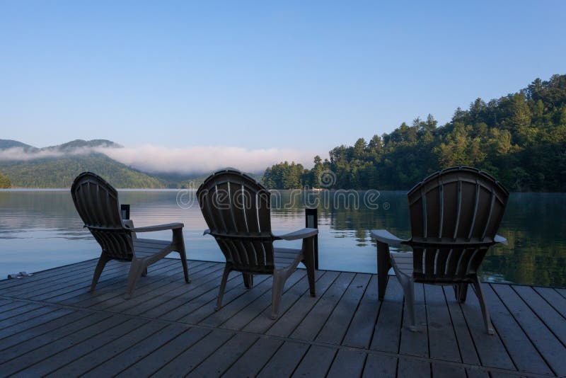 Adirondack sitzt auf einem Dock auf einem See am frühen Morgen vor