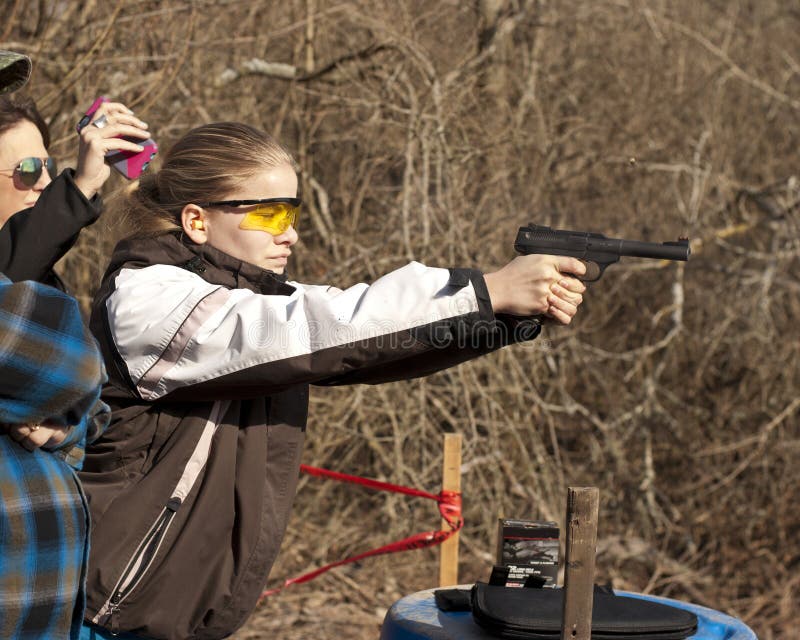 Adolescent girl shooting pistol with brass flying