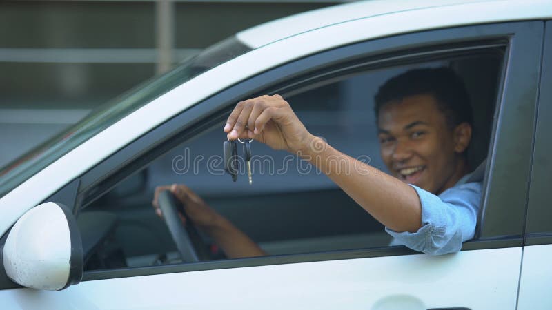 Adolescent heureux montrant la clé de la voiture à la fenêtre assis sur le siège du conducteur du véhicule neuf