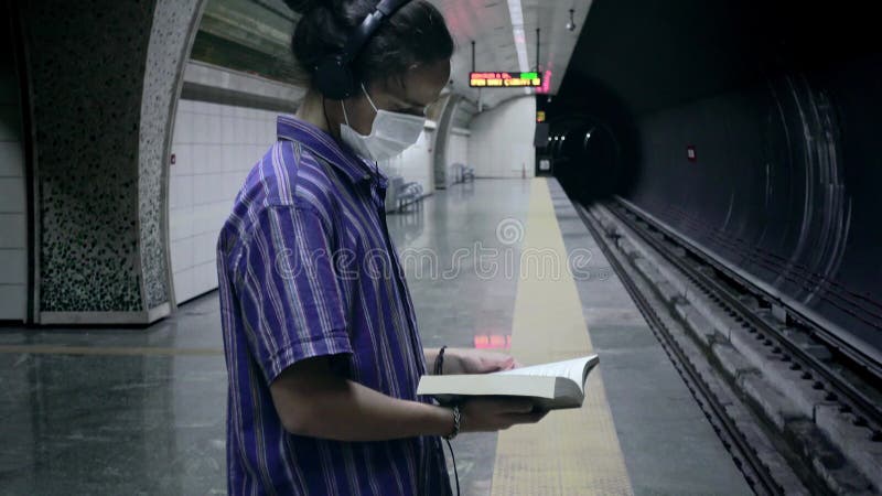 Adolescent masqué avec le livre de lecture d'écouteurs en attendant le métro à venir