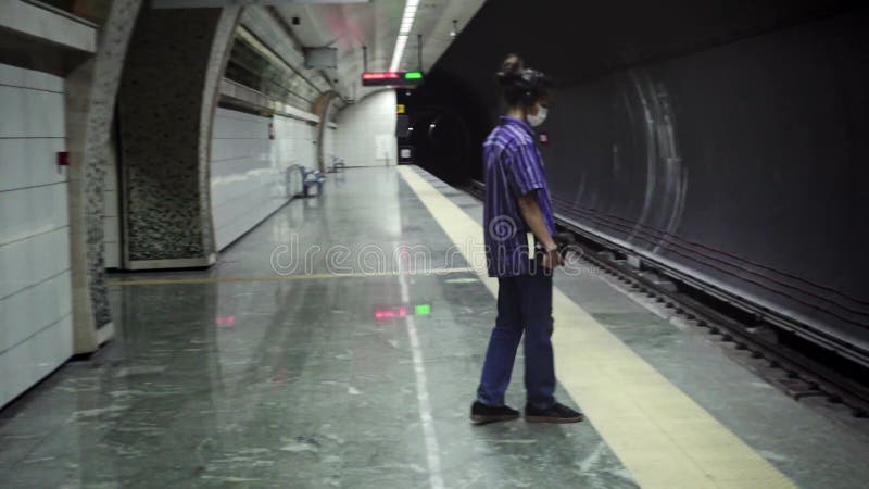 Adolescent masqué de marche avec le livre de lecture d'écouteurs en attendant le métro à venir