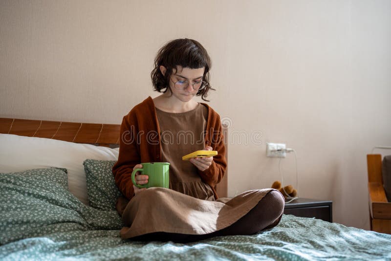 Adolescent pensif assis sur son lit avec une tasse de thé lire les nouvelles sur internet pendre sur le réseau social image libre de droits