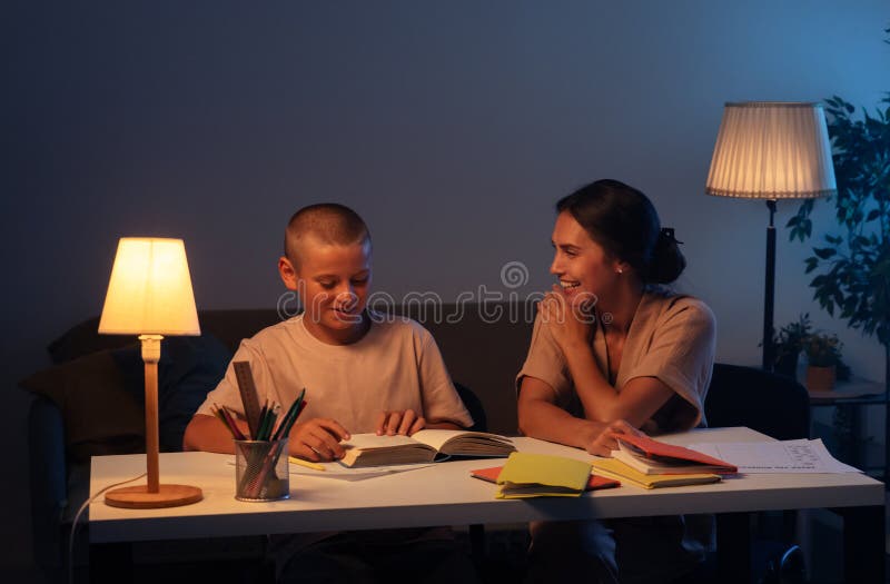 Adolescenta baiat este atent face temele sale fiu citind o carte mama sta langa fiu si uita cu zambet. Concept și educație royalty free stock image