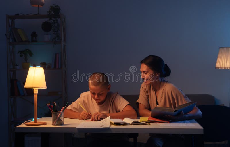 Adolescenta baiat este atent face temele sale în notebook mama deține o carte sits lângă fiu și ajuta cu atribuire. royalty free stock photo