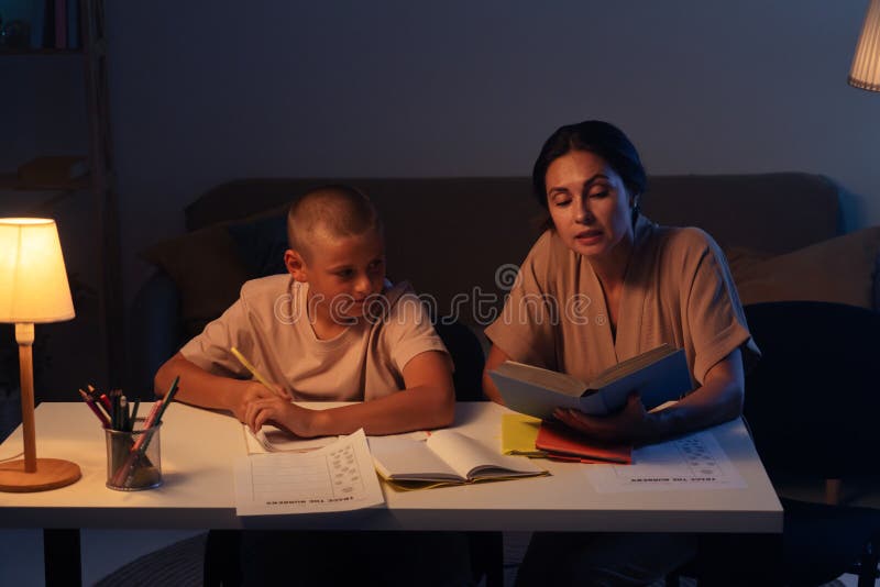 Adolescenta baiat este atent face temele sale în notebook mama deține o carte sits lângă fiu și dictând misiune. Concept stock image
