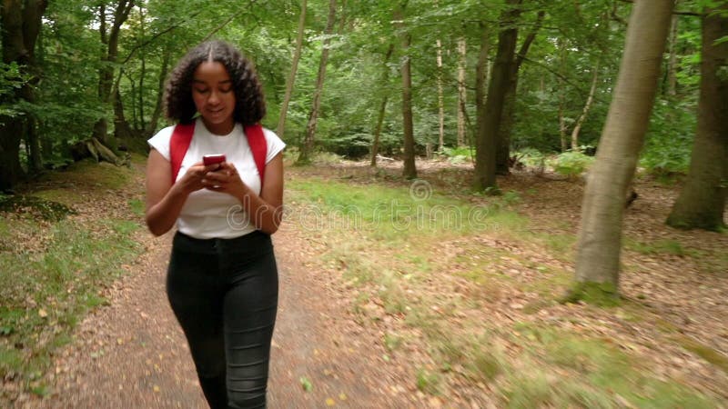 Adolescente afro-americana mestiça em uma floresta tirando fotos com celular