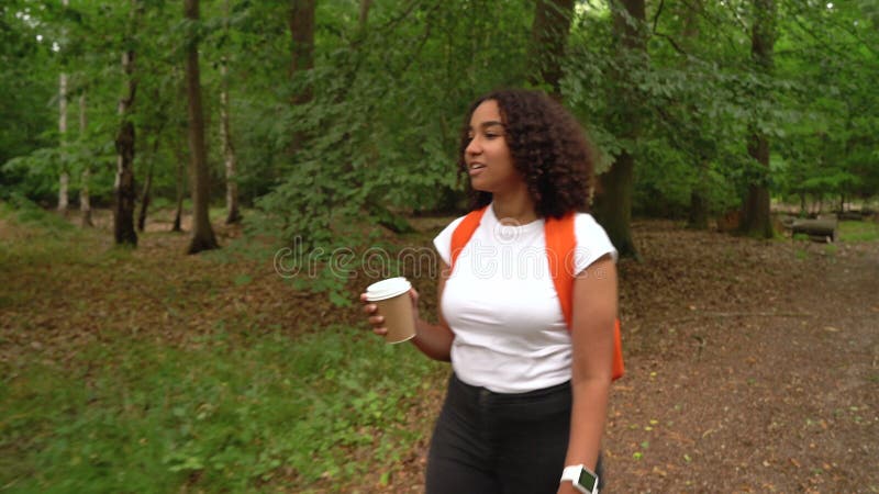 Adolescente afro-américaine métisse fille jeune femme randonnée avec sac à dos orange dans une forêt banque de vidéos