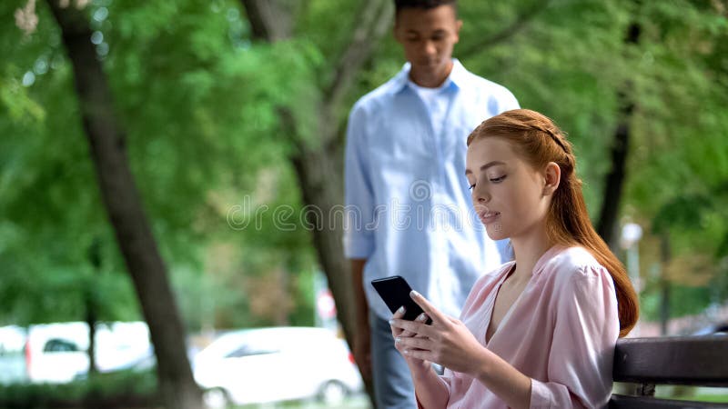 Adolescente afroamericano que se da cuenta de su novia chateando el smartphone, celos imagen de archivo libre de regalías