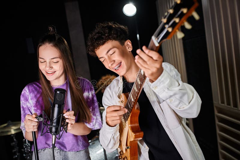 good looking cheerful teenage boy with braces playing guitar next to his cute vocalist in studio, stock photo. good looking cheerful teenage boy with braces playing guitar next to his cute vocalist in studio, stock photo