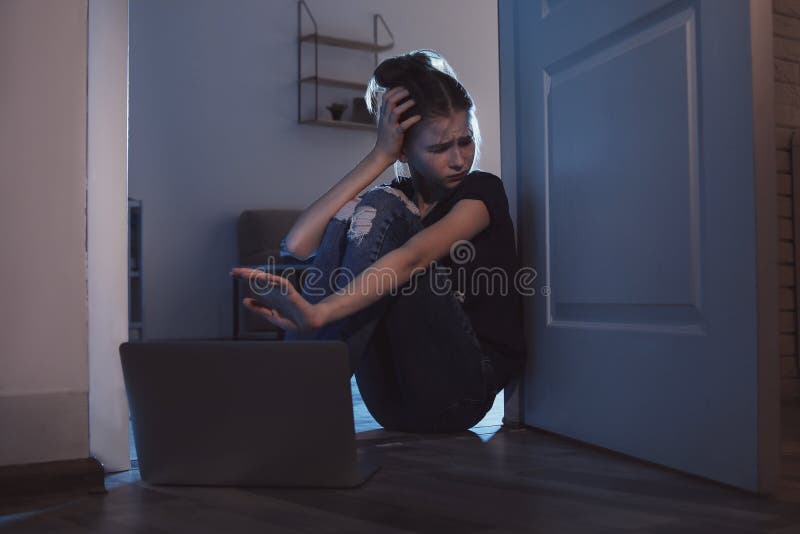 Adolescente amedrontado com o portátil no assoalho na sala escura imagens de stock Adolescente amedrontado com o portátil no assoalho na sala escura imagens de stock
