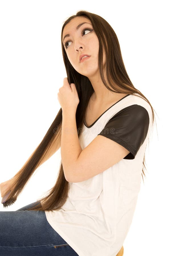 Asian American teen girl brushing her long dark hair with a brush looking up. Asian American teen girl brushing her long dark hair with a brush looking up