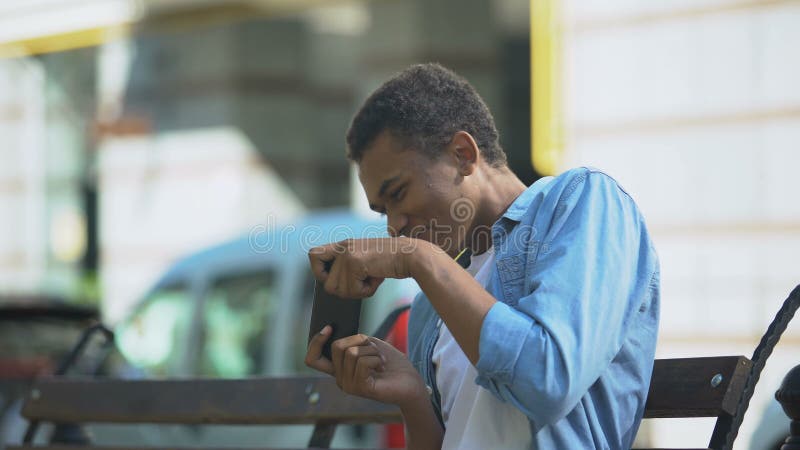 Adolescente animado jogando no smartphone sentado no banco, vício