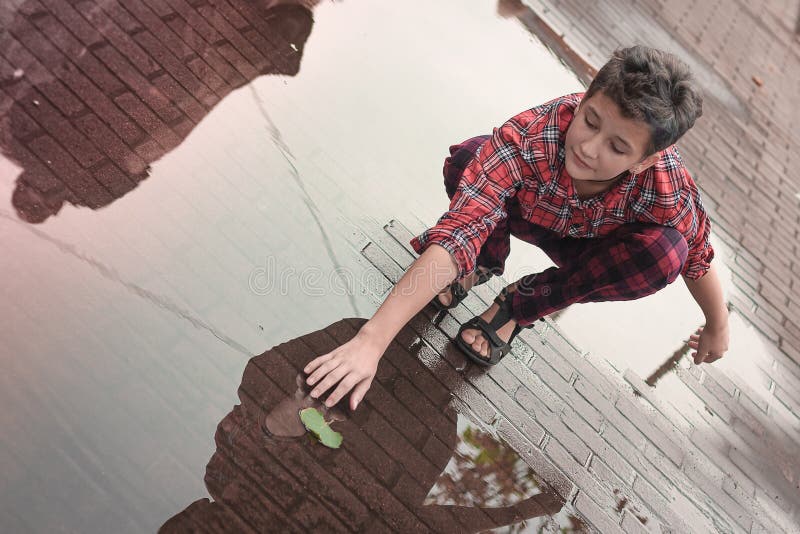 Young teen girl with short fashion haircut and hipster clothes catches a leaf from a puddle on a city street. Young teen girl with short fashion haircut and hipster clothes catches a leaf from a puddle on a city street