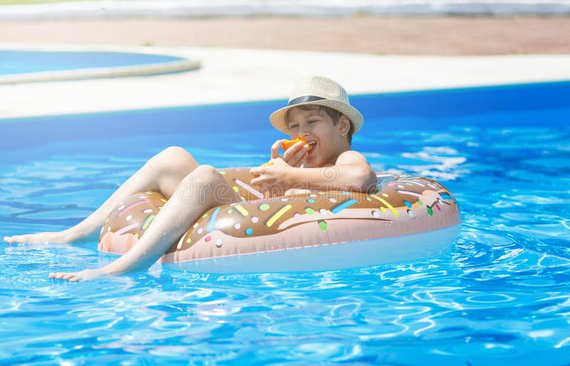 Adolescente bonito feliz do rapaz pequeno que encontra-se em um anel inflável da filhós na piscina Jogos ativos na água, férias, imagens de stock royalty free Adolescente bonito feliz do rapaz pequeno que encontra-se em um anel inflável da filhós na piscina Jogos ativos na água, férias, imagens de stock royalty free