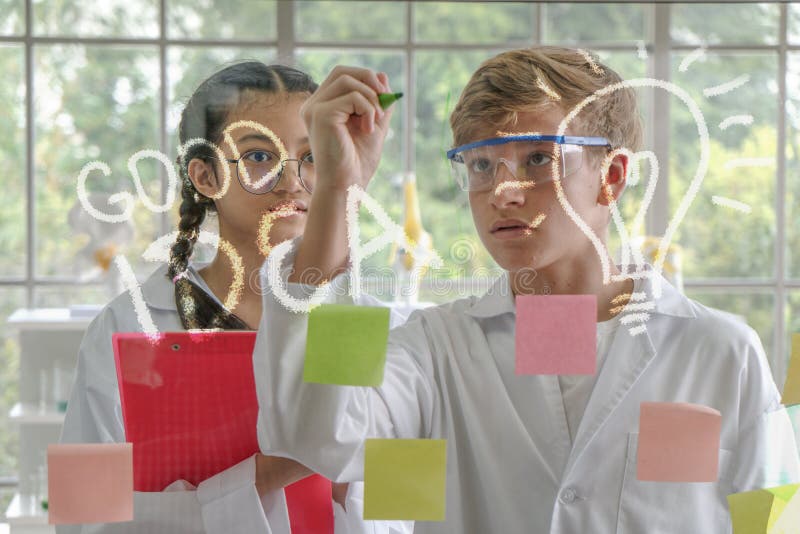 Adolescente caucasico e adolescente asiatico come ricercatori che scrivono le formule di matematica fotografia stock libera da diritti Adolescente caucasico e adolescente asiatico come ricercatori che scrivono le formule di matematica fotografia stock libera da diritti