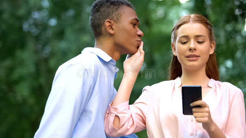 Adolescente chateando el smartphone rechazando el beso del novio mestizo, la adicción imagenes de archivo