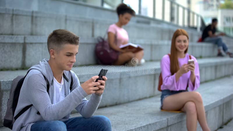 Adolescente chateando un smartphone junto a un compañero de clase, comunicación en línea imagen de archivo